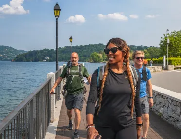 Three guests walking beside lake, road to their right.