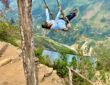 Guest on cliffside swing, overlooking large drop.
