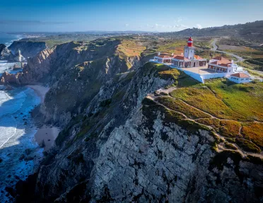 Wide shot of coastal cliffside, white and tan building.