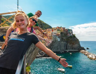 Three guests on cliff, gesturing towards colorful coastal city.
