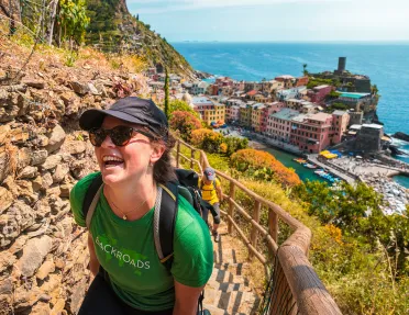 Two guests hiking up rocky trail, colorful coastal town in background.