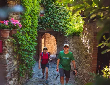 Two guests walking through arched brick walkway, flowers and hanging plants above.