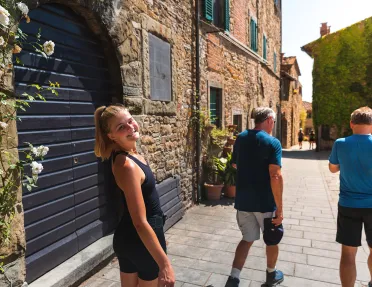 Three guests walking down brick road, one smiling at camera amidst storefronts.