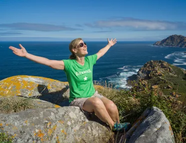 Guest on sunny hilltop, arms outstretched, ocean behind them.