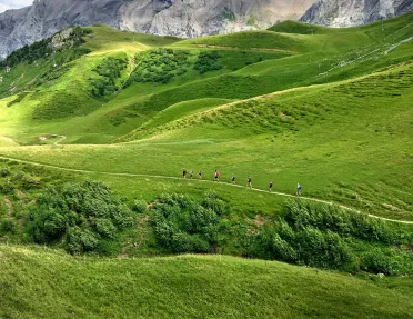 Side shot of guests walking on hilly meadow, mountains in distance. 