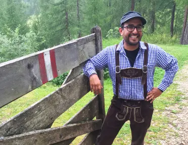 Local guide in traditional clothing posing for camera, leaning on wooden fence.
