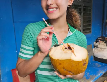 Woman holding up an opened coconut with a straw coming out of it