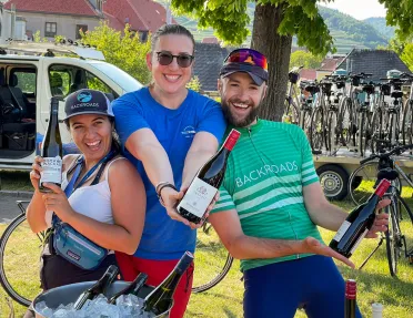 Two women and one man holding bottles of wine