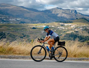 Woman smiling while biking on an asphalt road, with a large valley in the background
