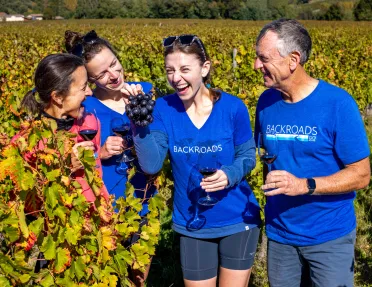 Group of people in a vineyard holding up bundles of grapes