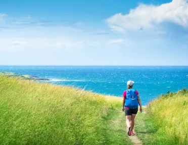 Woman hiking in a grassy field, with the ocean in the distance