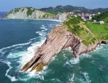 Slanted cliff on the coast of an ocean, with a small town in the distance