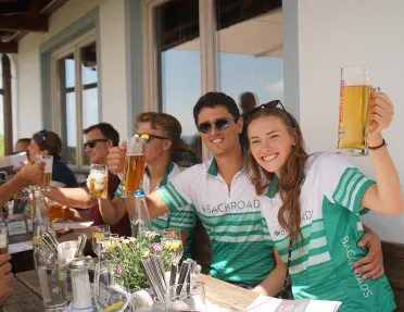 Man and women wearing a bicycle jersey, holding up glasses full of beer