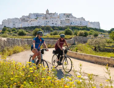 Two women riding bikes with an ancient building in the background