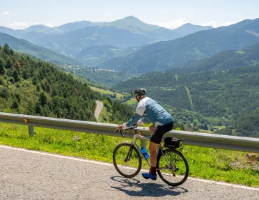 Man riding a bike on a road, with large valleys of trees in the distance with large hills