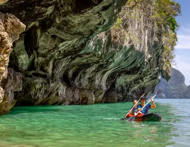 Man and woman paddling in a red kayak in the ocean, under a cliff