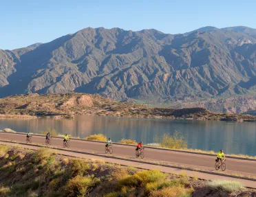 people biking down a road by a mountain range