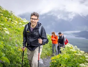 Man with walking sticks climbing up grassy hill