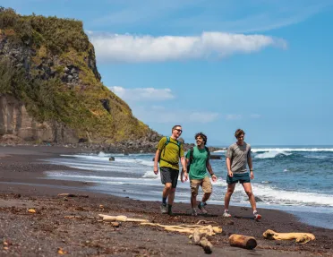Three men walking on a beach, with a large cliff in the background