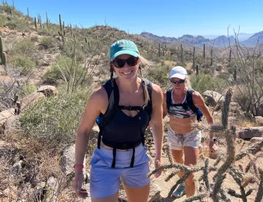 Two women smiling while walking though a desert full of cacti