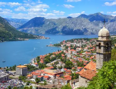 Aerial view of buildings all along the shore of a body of water, mountains in the distance