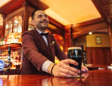 Man with a suit at a bar serving a glass of dark beer