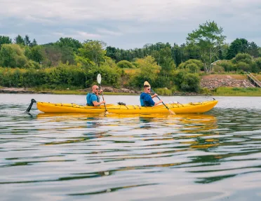 Two men inside of a yellow kayak, paddling in an open lake