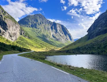 Asphalt road cutting through mountains with a lake to the right