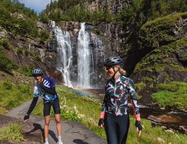 Two guests in cycling kits with a waterfall