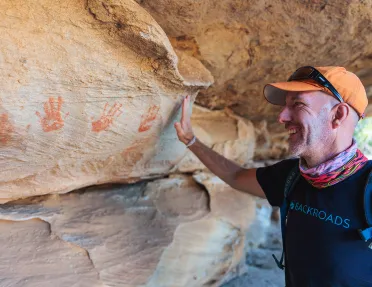 A man holds his hand up to handprints on a stone wall