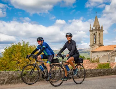 Man and woman biking on an asphalt road with a rustic clocktower in the background