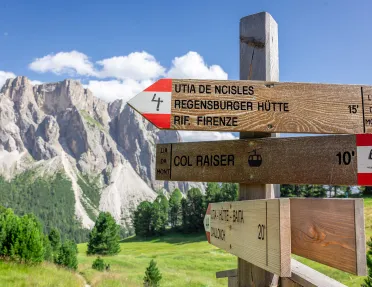 Wooden sign with red and white arrows, with tall rocky mountains in the background