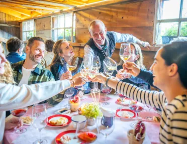 Group of people around a circular table, raising their wine glasses for a toast while smiling