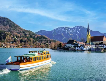 A small boat in the ocean heading towards buildings by a port