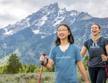 Woman and girl with walking poles hiking in a grassy valley