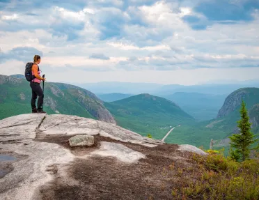 Woman at the top of a rock looking down at grassy hills