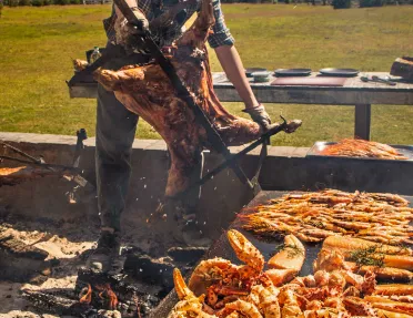 Man grilling seafood while carrying a pig on a rotisserie