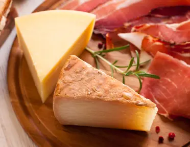 Wooden plank with two slices of cheese and various cured meats