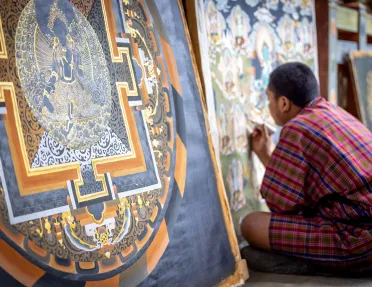 Man in monk attire painting a portrait while sitting on the ground