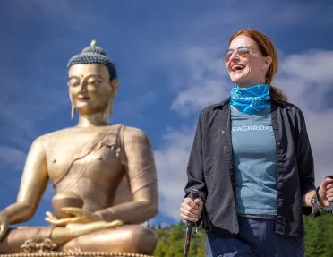Woman walking in front of a giant temple with a Buddhist statue in the background
