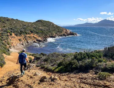 Man descending a dirt path towards a beach surrounded by trees
