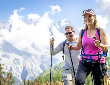 Man and woman with walking poles ascending a grassy mountain