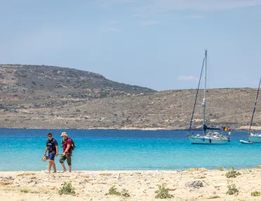 Two people on the beach walking next to the ocean with their shoes in hand