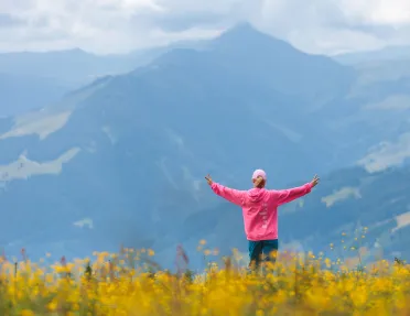 Woman wearing a pink jacket on top of a hill with her arms open