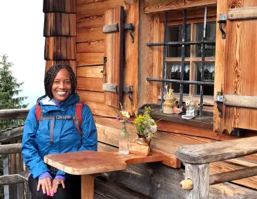 A person poses in front of a wooden house