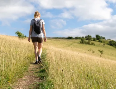 Woman walking through a field of tall weeds in a valley