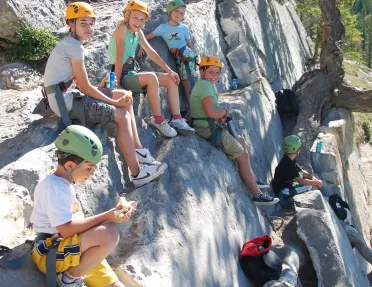 Group of kids sitting on a large boulder with climbing gear on