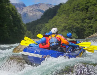 Group of people on a blue raft, paddling through an active river