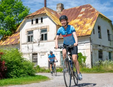 Woman smiling while riding a bike on a gravel road, with an old shed in the background