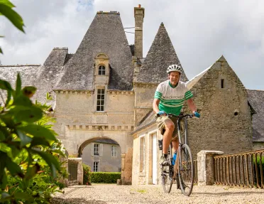 Man smiling while riding a bike with a stone castle in the background